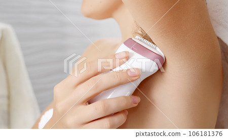 Young woman using electric epilator to remove armpit hair in bathroom 106181376