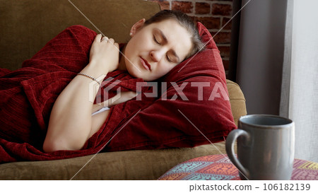 Young sick woman covering in plaid on sofa and coughing. Healthcare, female feeling sick at home, illness and health problems. Young sick woman covering in plaid on sofa and coughing. Healthcare, female feeling sick at home, illness and health problems. 106182139