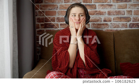 Portrait of thoughtful sad woman sitting on sofa and listening music in headphones. People relaxing at home, having fun, positive emotions and joy. Portrait of thoughtful sad woman sitting on sofa and listening music in headphones. People relaxing at home, having fun, positive emotions and joy. 106182625