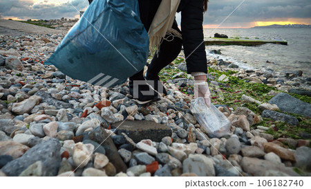 Closeup of female volunteer picking up plastic garbage on rocky sea beach Closeup of female volunteer picking up plastic garbage on rocky sea beach 106182740