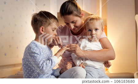 Smiling mother cutting fingernails to her two sons wearing pajamas at night. Parenting, child hygiene and healthcare, going to sleep. Smiling mother cutting fingernails to her two sons wearing pajamas at night. Parenting, child hygiene and healthcare, going to sleep. 106183680