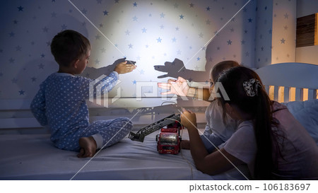 Happy kids with mother playing with flashlight in shadow theater at night Happy kids with mother playing with flashlight in shadow theater at night 106183697