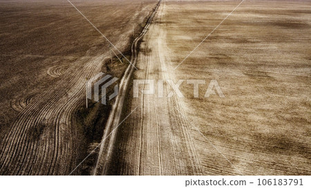 Dirt road between arable fields, aerial view. Landscape. Arable fields in the spring. Power line poles. Dirt road between arable fields, aerial view. Landscape. Arable fields in the spring. Power line poles. 106183791