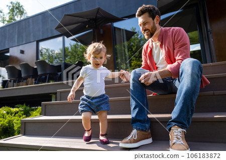 Dad and little son sitting on the steps and looking contented Dad and little son sitting on the steps and looking contented 106183872
