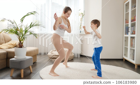 Cheerful mother and 6 year old son dancing at home together. Family having fun together, listening music, active lifestyle, parenting and child development Cheerful mother and 6 year old son dancing at home together. Family having fun together, listening music, active lifestyle, parenting and child development 106183980