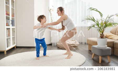 Happy smiling mother playing and dancing with her little son in living room at home. Family having fun together, listening music, active lifestyle, parenting and child development 106183981