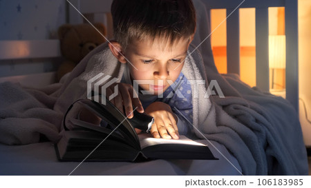 Cute boy in pajamas reading a book with flashlight in bed. Children education, development, secrecy, reading books. Cute boy in pajamas reading a book with flashlight in bed. Children education, development, secrecy, reading books. 106183985