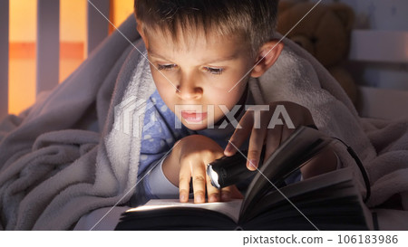 Closeup of boy holding flashlight reading book in bed. Children education, development, secrecy, privacy, reading books. Closeup of boy holding flashlight reading book in bed. Children education, development, secrecy, privacy, reading books. 106183986
