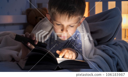 Portrait of boy with torch lying in bed and reading story book. Children education, development, secrecy, privacy, reading books. Portrait of boy with torch lying in bed and reading story book. Children education, development, secrecy, privacy, reading books. 106183987