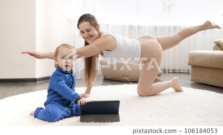 Happy smiling mother with babyy son doing fitness exercise and watching online training n tablet computer 106184053