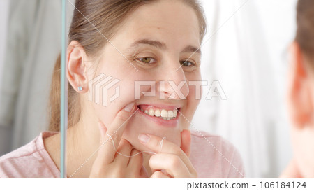 Closeup of young woman checking her teeth after cleaning them with dental floss 106184124