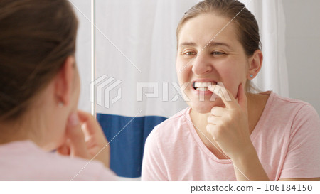 Beautiful smiling woman looking at her reflection in mirror and rubbing off the tooth plaque. Concept of teeth health, self checking mouth and oral hygiene. Beautiful smiling woman looking at her reflection in mirror and rubbing off the tooth plaque. Concept of teeth health, self checking mouth and oral hygiene. 106184150