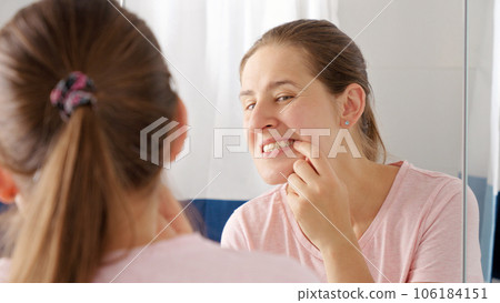 Portrait of smiling young woman opens mouth and looks at the reflection of her teeth in mirror. Concept of teeth health, self checking mouth and oral hygiene. Portrait of smiling young woman opens mouth and looks at the reflection of her teeth in mirror. Concept of teeth health, self checking mouth and oral hygiene. 106184151