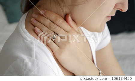 Closeup of young woman sitting on bed and rubbing her aching neck in morning. Concept of healthcare problems, pain relief and injuries. Closeup of young woman sitting on bed and rubbing her aching neck in morning. Concept of healthcare problems, pain relief and injuries. 106184430