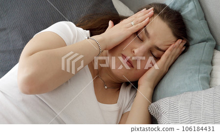 Portrait of young woman lying in bed and suffering from headache. Concept of healthcare problems, pain relief and hangover. Portrait of young woman lying in bed and suffering from headache. Concept of healthcare problems, pain relief and hangover. 106184431