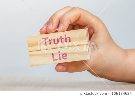Truth and lie. A hand holds two wooden cubes with the inscriptions TRUTH and LIE To be inserted into a design or project. 106184624