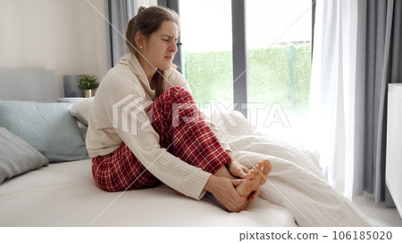 Young woman sitting in bed and massaging her aching feet because of muscle cramp Young woman sitting in bed and massaging her aching feet because of muscle cramp 106185020