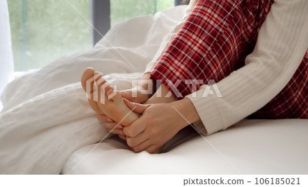 Closeup of woman massaging and holding her feet after feeling pain because of muscle cramp while lying in bed. Concept of injury, health problems, pain and trauma. Closeup of woman massaging and holding her feet after feeling pain because of muscle cramp while lying in bed. Concept of injury, health problems, pain and trauma. 106185021