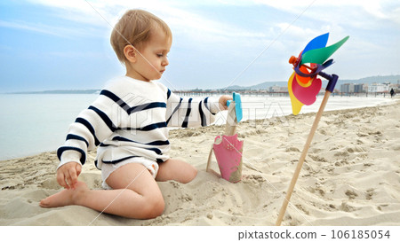 Cute little baby boy digging sand on the sea beach with a shovel. Joy and happiness of a family journey, weekend getaway, and vacation. 106185054