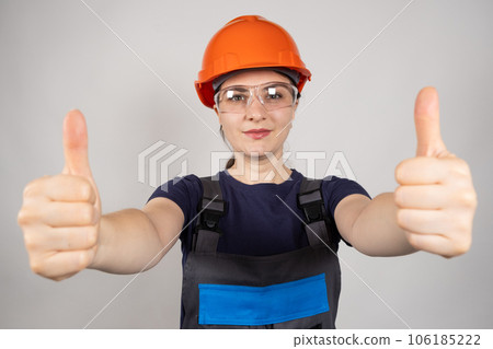 A female construction worker or engineer wearing a helmet and glasses shows thumbs up on a white background. A female construction worker or engineer wearing a helmet and glasses shows thumbs up on a white background. 106185222