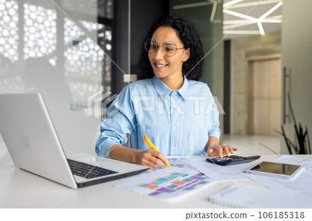 Successful business woman financier on paper work with contracts, reports works sitting at workplace,hispanic smiling uses calculator and laptop, female employee satisfied with achievement results Successful business woman financier on paper work with contracts, reports works sitting at workplace,hispanic smiling uses calculator and laptop, female employee satisfied with achievement results 106185318