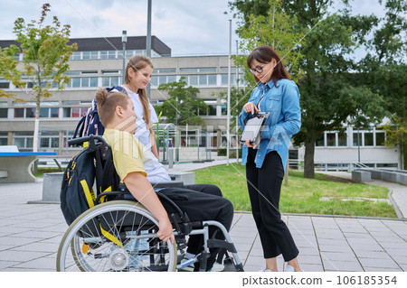 Female teacher and children, boy in wheelchair and girl talking outdoor 106185354