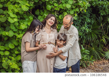 A loving family enjoying a leisurely walk in the park - a radiant pregnant woman after 40, embraced by her husband, and accompanied by their adult teenage children, savoring precious moments together A loving family enjoying a leisurely walk in the park - a radiant pregnant woman after 40, embraced by her husband, and accompanied by their adult teenage children, savoring precious moments together 106186548