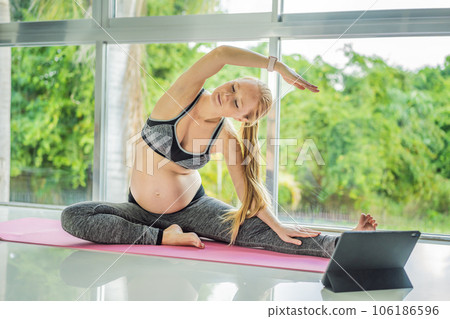 Portrait of young pregnant woman doing yoga on mat with online video lessons indoors on a daytime. Balance exercises. Motherhood, health care, sportive lifestyle, fitness, wellness, pregnancy concept 106186596