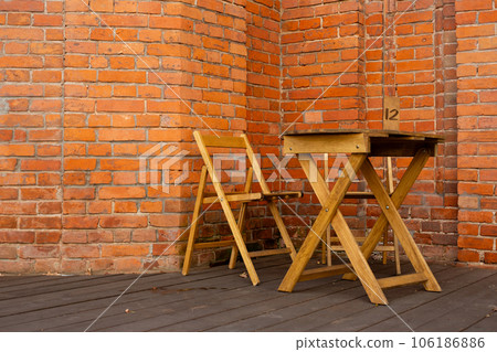 Wooden terrace with a table and a chair against the background of a brick building with a sign with a table number for reservation table in a summer cafe 106186886
