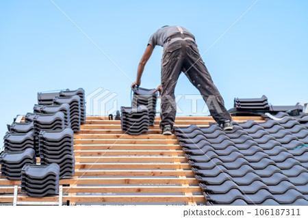 a craftsman installs a fired ceramic tile on the roof of family house a craftsman installs a fired ceramic tile on the roof of family house 106187311