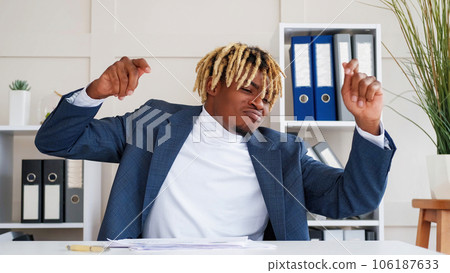 Enjoying work. Success celebration. Smiling positive happy business man in suit sitting at desk dancing hands up in light modern office interior. 106187633