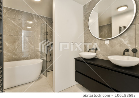 a modern bathroom with two sinks and a large round mirror above the sink is in front of the bathtub 106188692