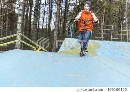 A happy Boy rides a stunt scooter in a skatepark. A happy Boy rides a stunt scooter in a skatepark. 106190125