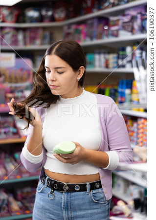 Happy young woman choosing hair shampoo or conditioner in cosmetics shop Happy young woman choosing hair shampoo or conditioner in cosmetics shop 106190377
