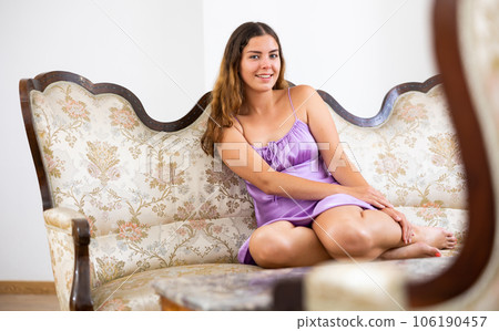 Smiling woman in purple nightgown posing on luxurious couch at home 106190457