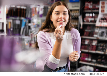 Positive girl testing new lipstick in cosmetics shop 106190474