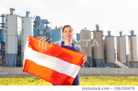 near suburban factory,female worker in overalls is delighted stands and holds Austrian flag in hands 106190476