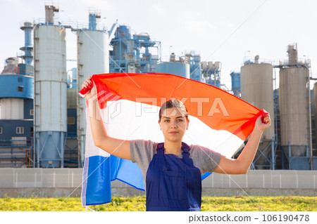 Calm young woman worker with flag of Holland against background of factory Calm young woman worker with flag of Holland against background of factory 106190478
