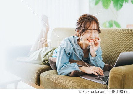 A woman using a computer while lying on the sofa 106190553