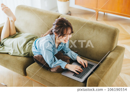 A woman using a computer while lying on the sofa 106190554