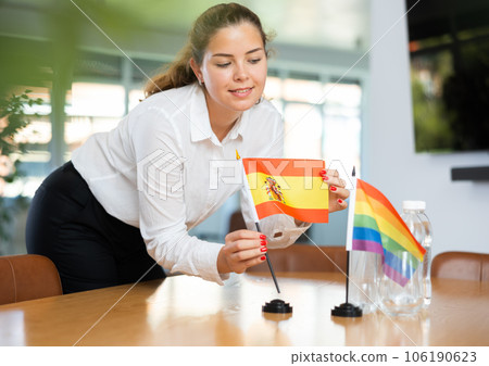 Young woman putting Spain and LGBT flags on table in office Young woman putting Spain and LGBT flags on table in office 106190623
