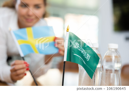 Little flag of Saudi Arabia on table and flag of Sweden put next to it by young woman 106190645