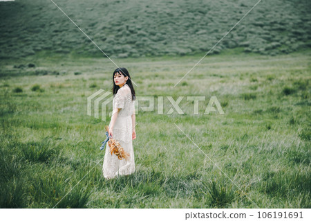 一個穿著白色連衣裙的女人在草地上拿著花束 106191691