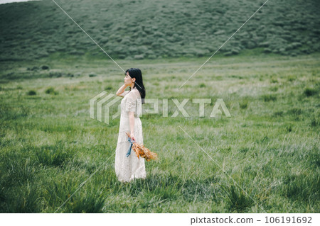 一個穿著白色連衣裙的女人在草地上拿著花束 106191692