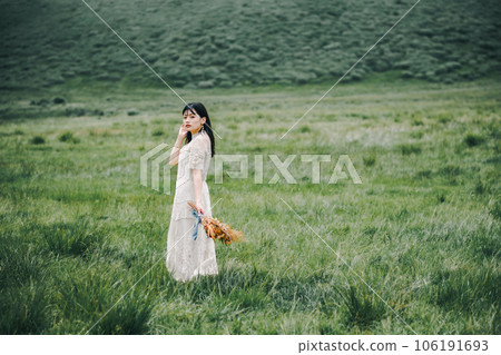 一個穿著白色連衣裙的女人在草地上拿著花束 106191693