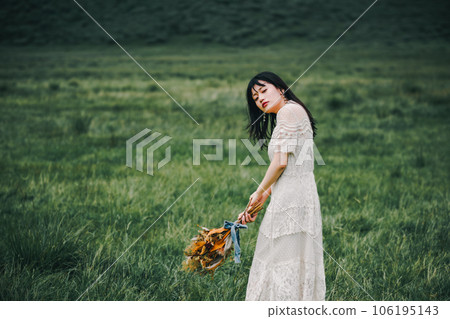 A woman in a white dress holding a bouquet in the meadow A woman in a white dress holding a bouquet in the meadow 106195143