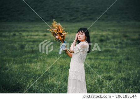 A woman in a white dress holding a bouquet in the meadow A woman in a white dress holding a bouquet in the meadow 106195144