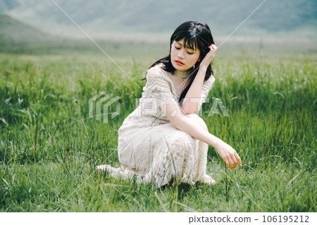 一個穿著白色連衣裙的女人蹲在草地上 一個穿著白色連衣裙的女人蹲在草地上 106195212