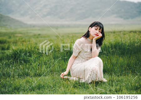 A woman in a white dress crouching on a meadow 106195256