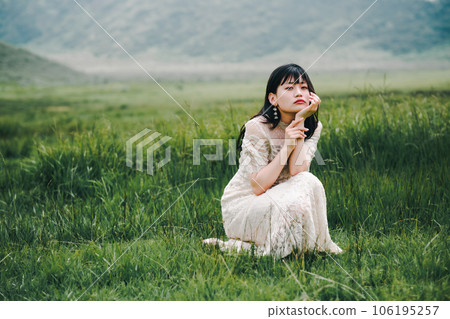 A woman in a white dress crouching on a meadow A woman in a white dress crouching on a meadow 106195257